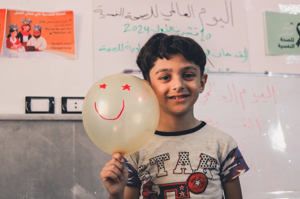 Child holding a smiley balloon, promoting mental health awareness in a classroom setting.